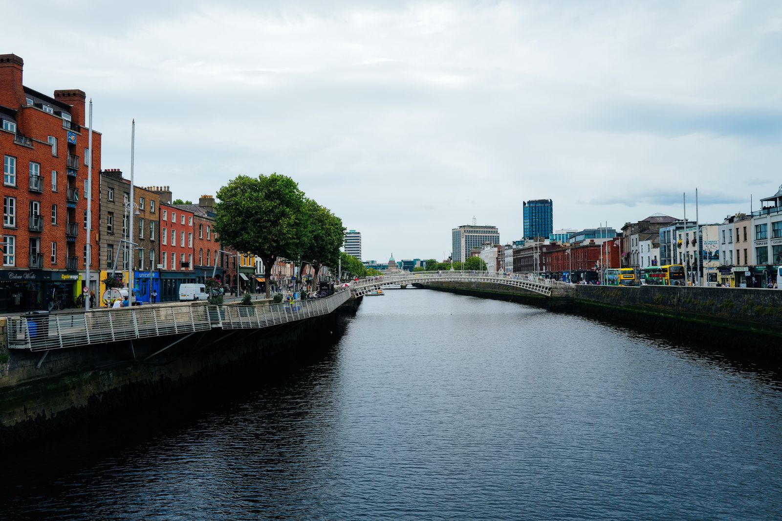 Scenic view of Dublin's Ha'penny Bridge over the River Liffey amidst urban architecture and vibrant city life.