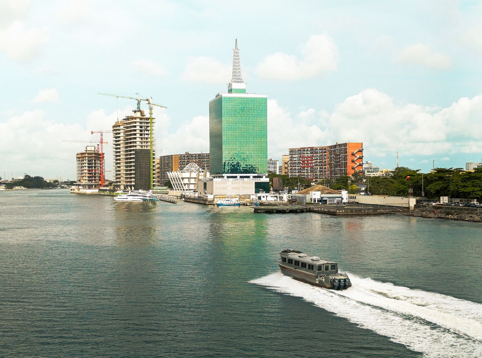 Scenic view of Lagos skyline featuring modern buildings and a motorboat in the lagoon under a bright sky.