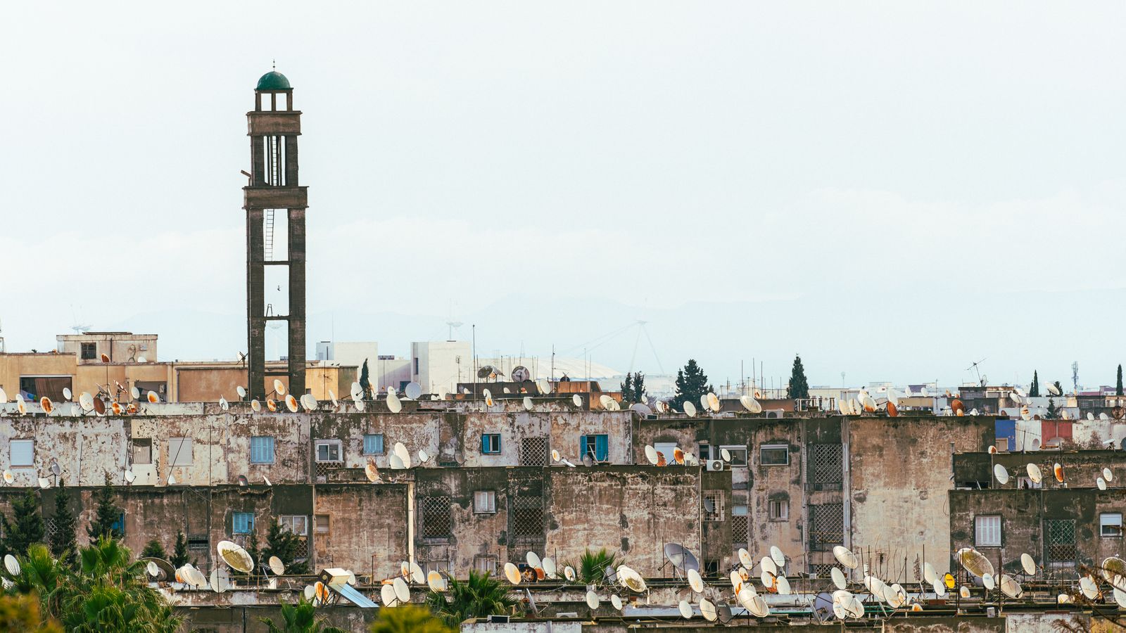 Urban rooftops with satellite dishes beneath a towering minaret in Tunis, Tunisia.