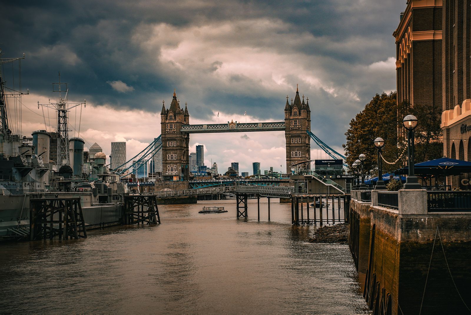 Moody view of London's Tower Bridge under cloudy skies, showcasing the city's historic architecture and urban skyline.
